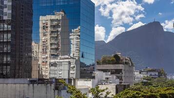 A modern building with a glass facade, surrounded by lush greenery and a mountainous backdrop.