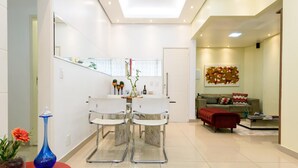 A modern living room with a sofa, a red ottoman, and a coffee table. There is a dining area with two white chairs and a table. - Style in Ipanema Good Location Vp305 (Rio de Janeiro)