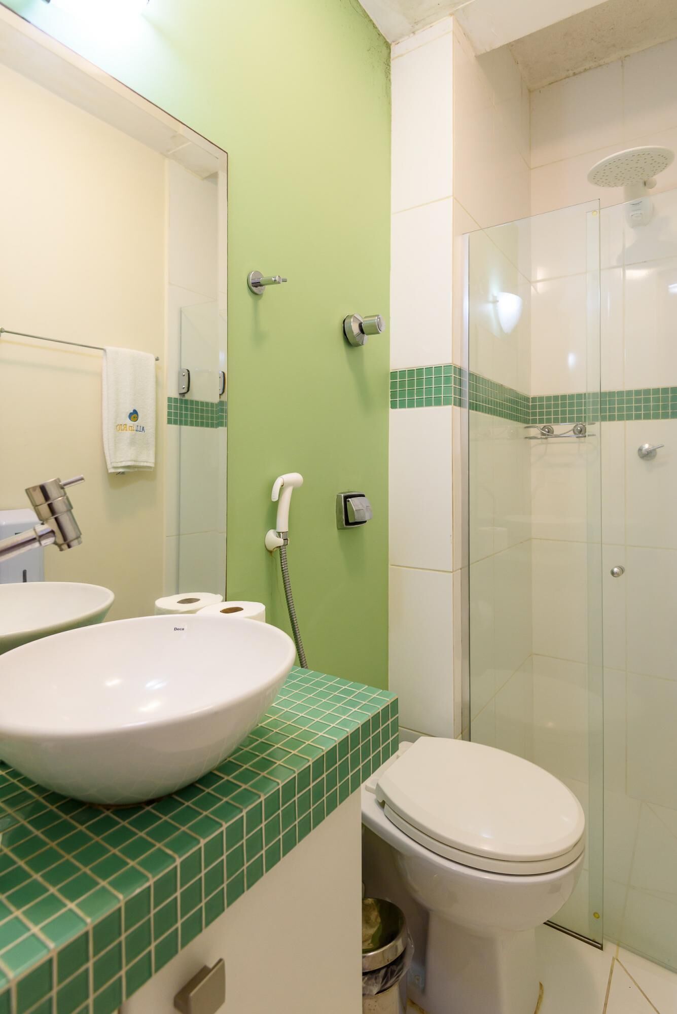 A bathroom with a green-tiled vanity, a white sink, and a toilet.
