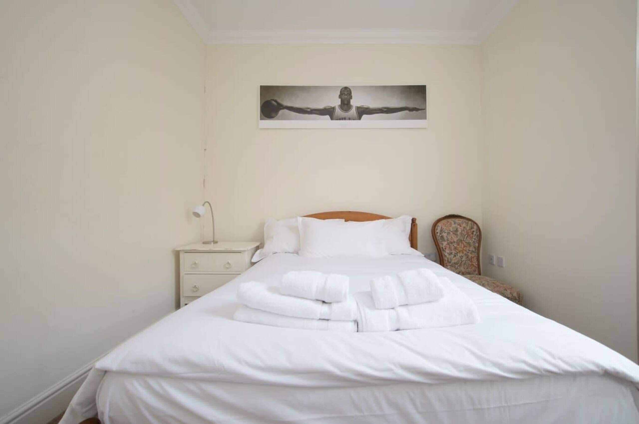 A neatly made bed with white linens and towels, a nightstand with a lamp, and a chair with a floral pattern.