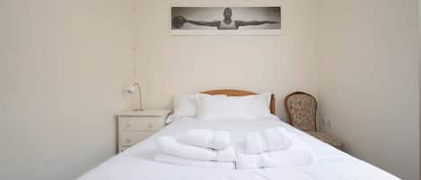 A neatly made bed with white linens and towels, a nightstand with a lamp, and a chair with a floral pattern.
