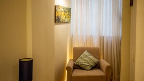 A room with a beige armchair, a lamp, and a painting on the wall.