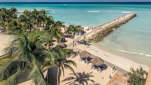 Een strand met helder turquoise water, palmbomen en een lange pier die in zee reikt.