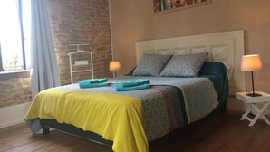 A bedroom with a bed, two bedside lamps, a window with curtains, a wall-mounted painting, and a wooden floor.