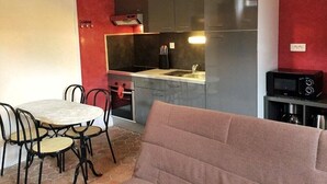 A compact kitchen with grey cabinets, a dining table with chairs, and a microwave on a small table.