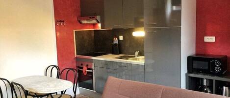 A compact kitchen with grey cabinets, a dining table with chairs, and a microwave on a small table.