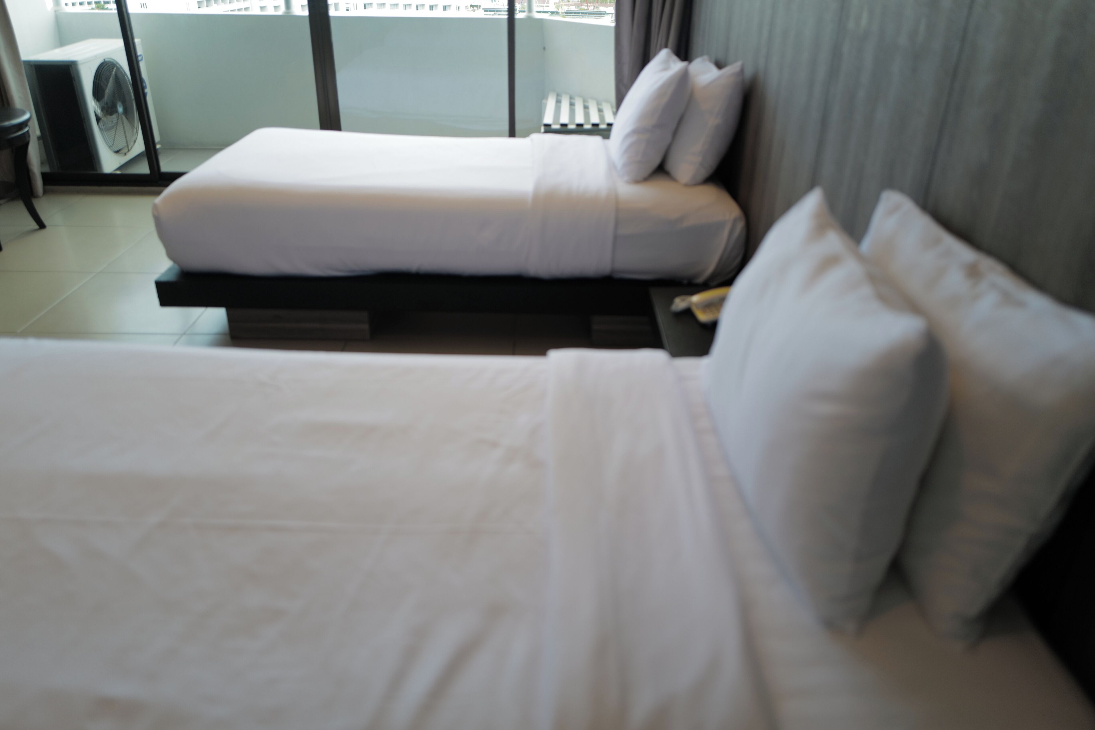 A hotel room with a bed, pillows, a small table, and a window with a view of the city.
