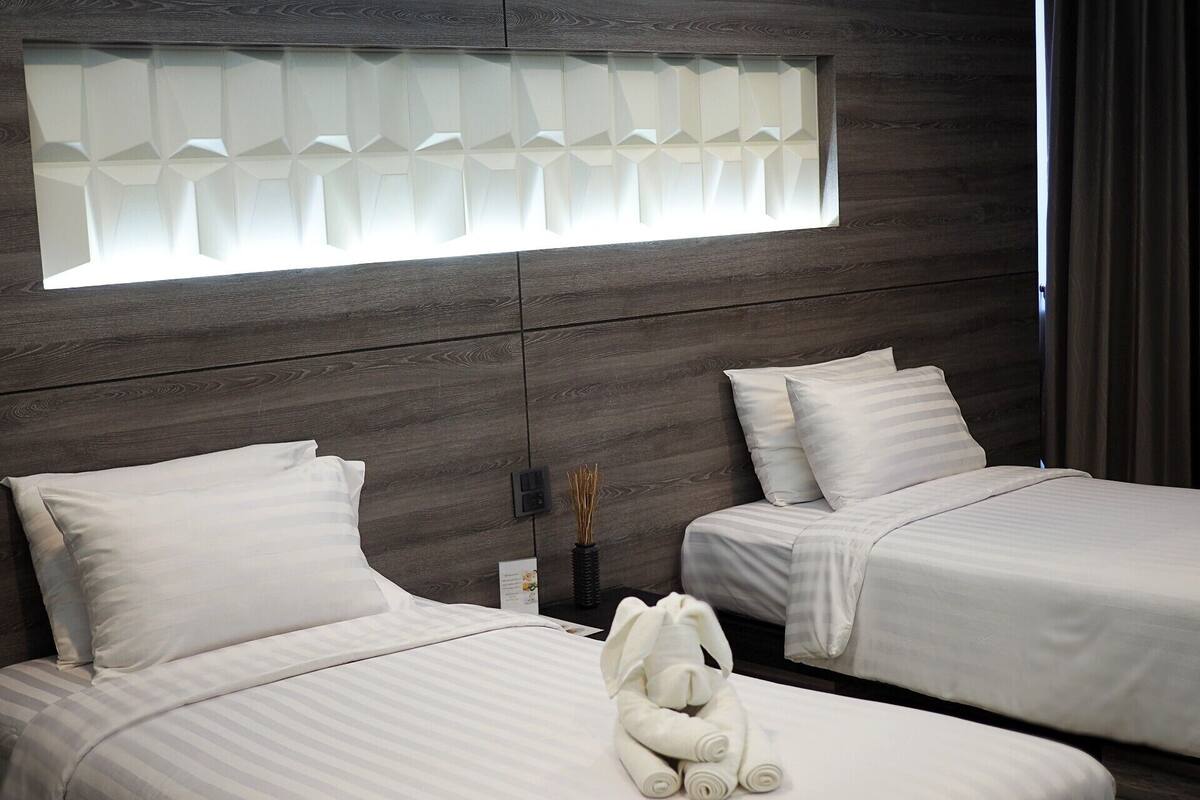A hotel room with two beds, a window with a geometric pattern, and a teddy bear on the bed.