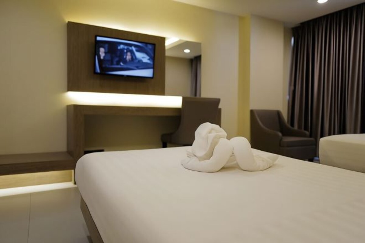 A hotel room with a large bed, a flat-screen TV mounted on the wall, and two armchairs.