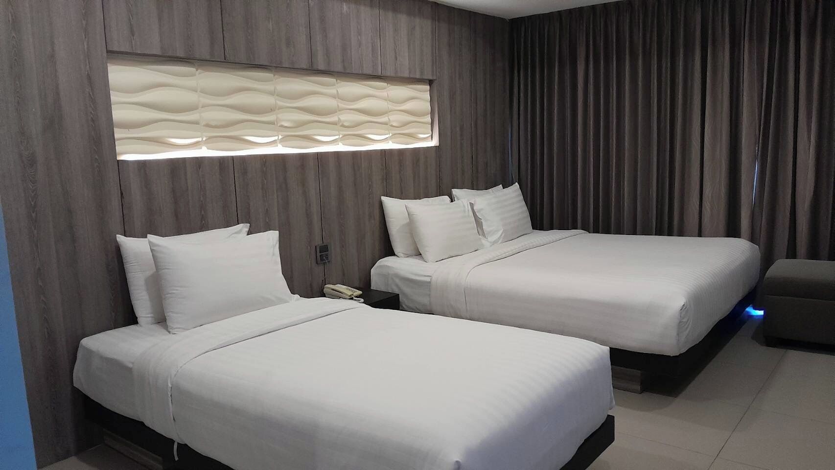 A hotel room with two beds, a modern light fixture, and a curtain.