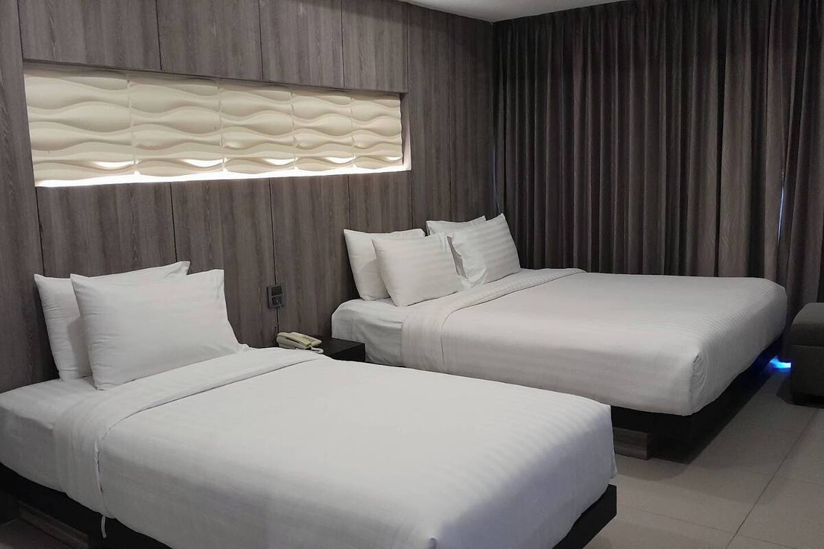 A hotel room with two beds, a modern light fixture, and a curtain.