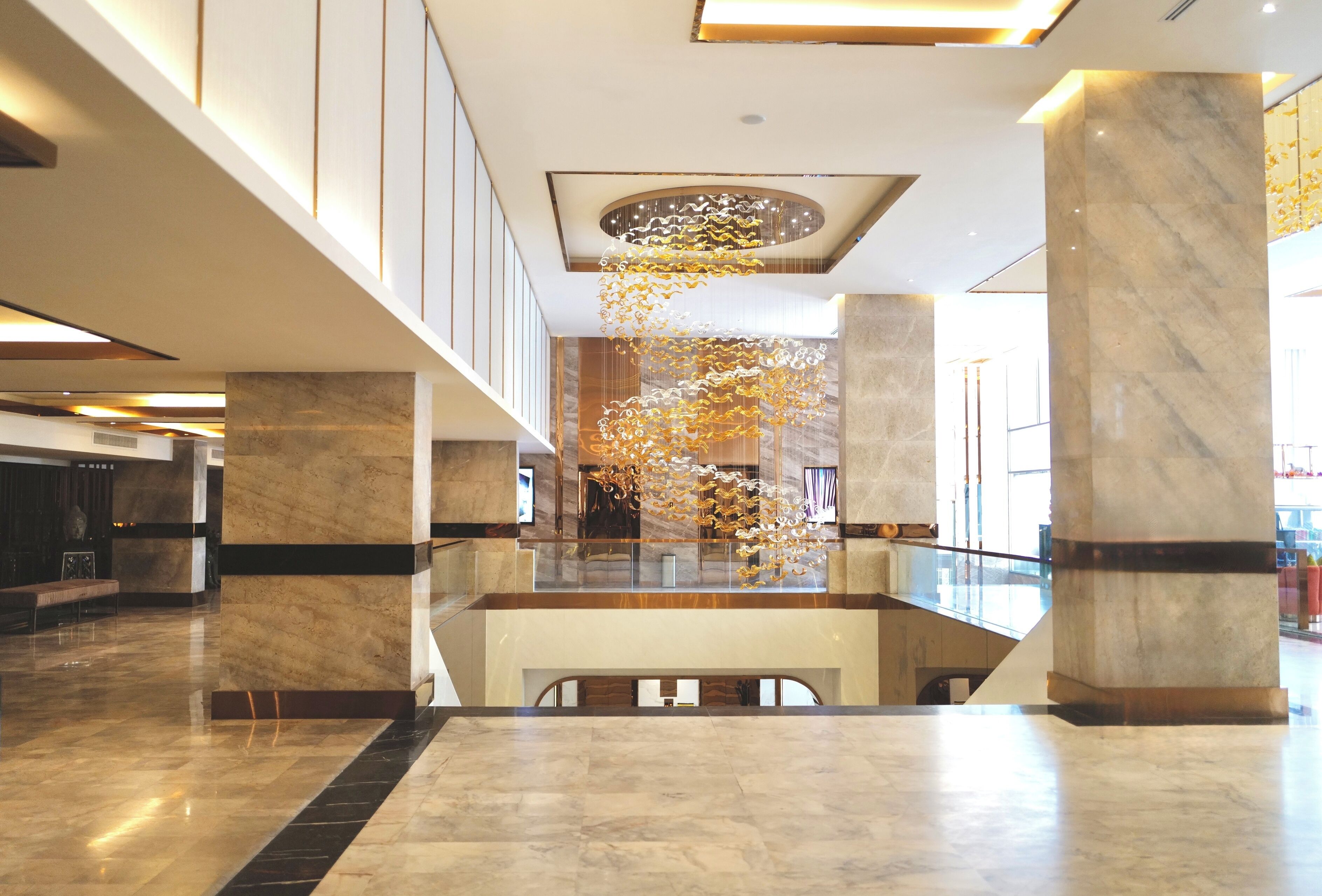 Un lobby amplio con suelo de mármol, una escalera central y un candelabro decorativo.