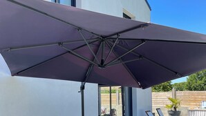 An outdoor patio with a wooden table and chairs, a large umbrella, and potted plants.