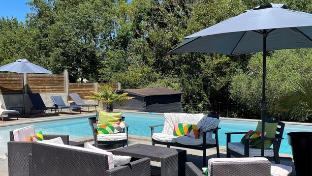 A poolside area with wicker furniture, colorful cushions, and a large umbrella.