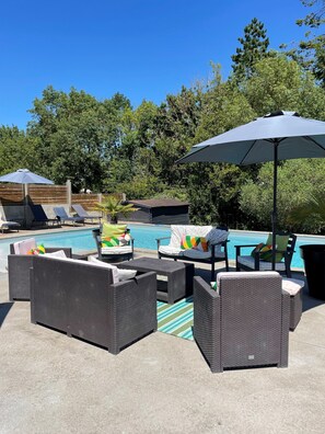 A poolside area with wicker furniture, colorful cushions, and a large umbrella.