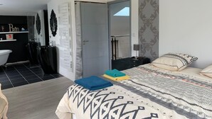 A bedroom with a bed, a bedside table, a nightstand, a bathroom with a sink and mirror, and a small balcony.