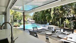 Ett modernt utomhusområde med plats för måltider, en pool och tropisk växtlighet.