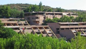 A cluster of buildings with multiple levels, surrounded by greenery and hills.