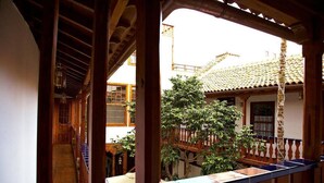 A wooden interior corridor with a view of a courtyard featuring a tiled-roof building, a wooden balcony, and a tree. - Emblematico San Agustin Hotel (Icod de los Vinos)