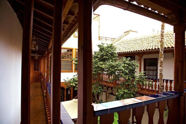 A wooden interior corridor with a view of a courtyard featuring a tiled-roof building, a wooden balcony, and a tree. - Emblematico San Agustin Hotel (Icod de los Vinos)