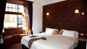 A hotel room with a large bed, wooden bench, two bedside lamps, and a patterned wallpaper. - Emblematico San Agustin Hotel (Icod de los Vinos)