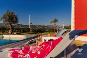 A poolside lounge area with a view of the landscape, a table with drinks, and a bag on the table. - Villa Clara - Country Retreat (Solarino)