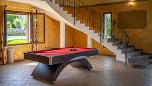 Una mesa de billar en una habitación con una escalera y un ventanal con cortinas.