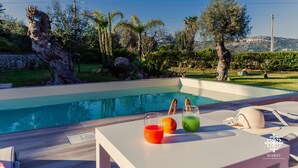 Un área junto a la piscina con una terraza de madera, una mesa con bebidas y vistas a la piscina y la vegetación circundante.