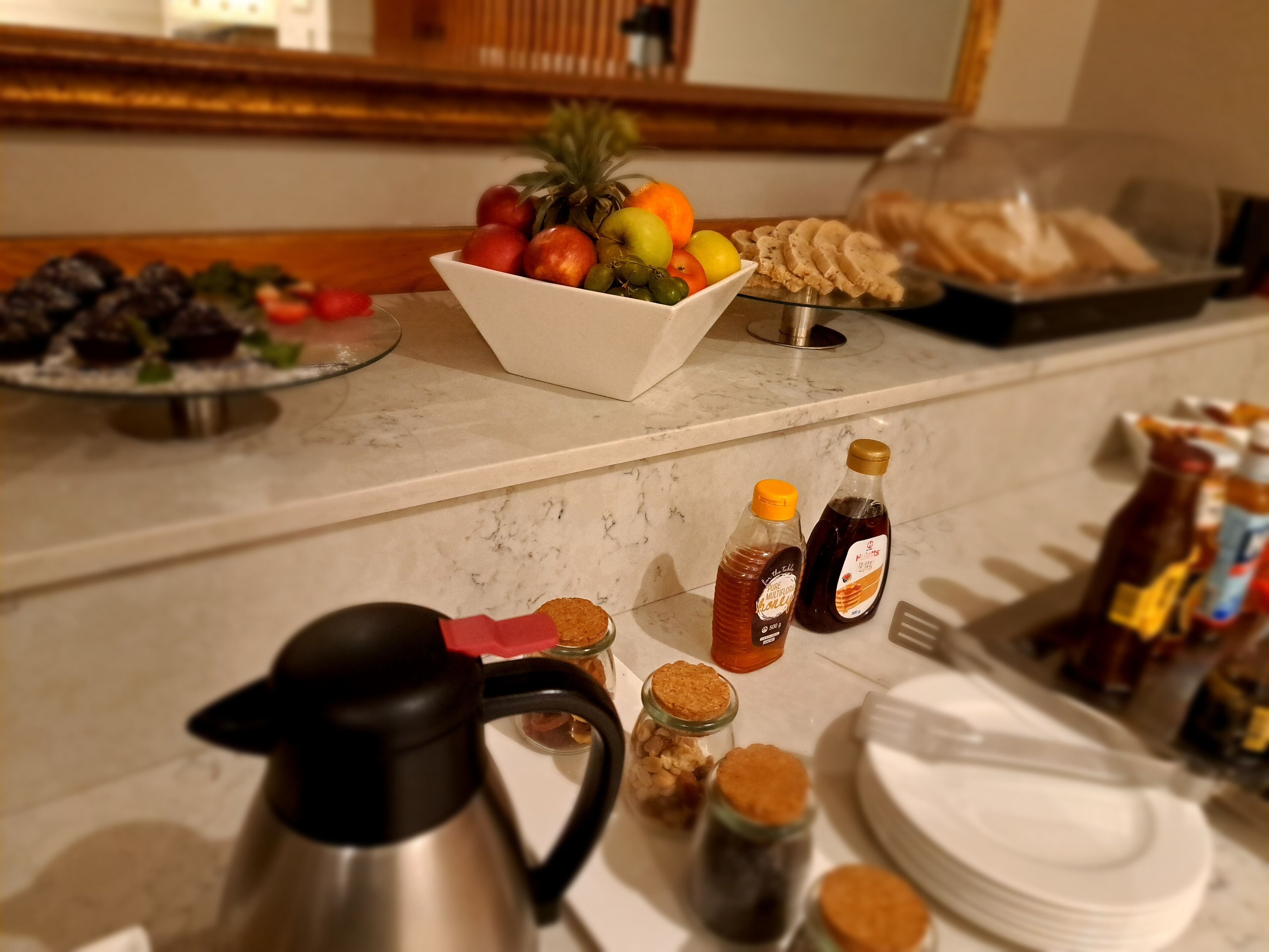 A breakfast buffet with fruits, pastries, and condiments on a marble countertop.