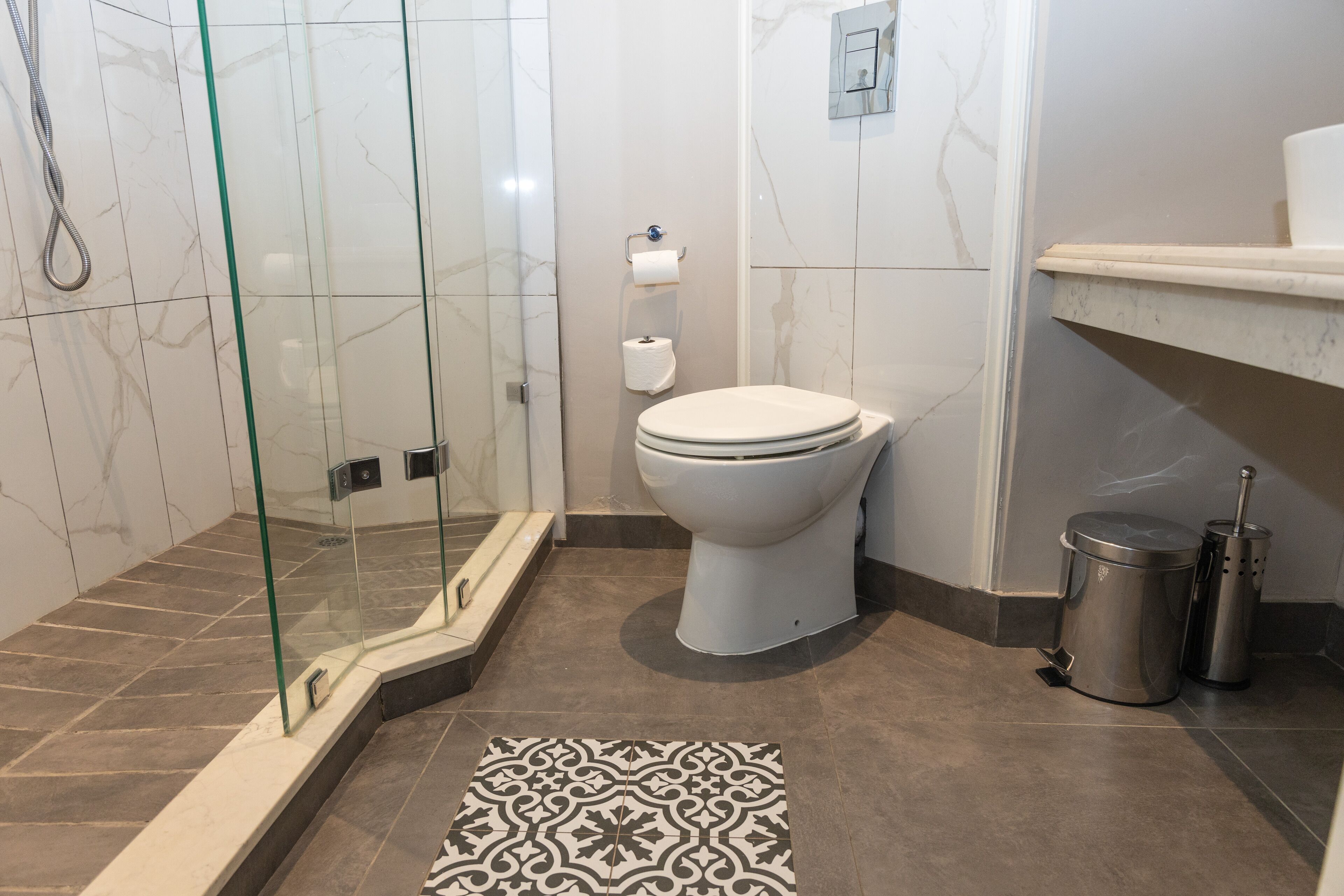A modern bathroom with a glass-enclosed shower, a toilet, and a trash bin.