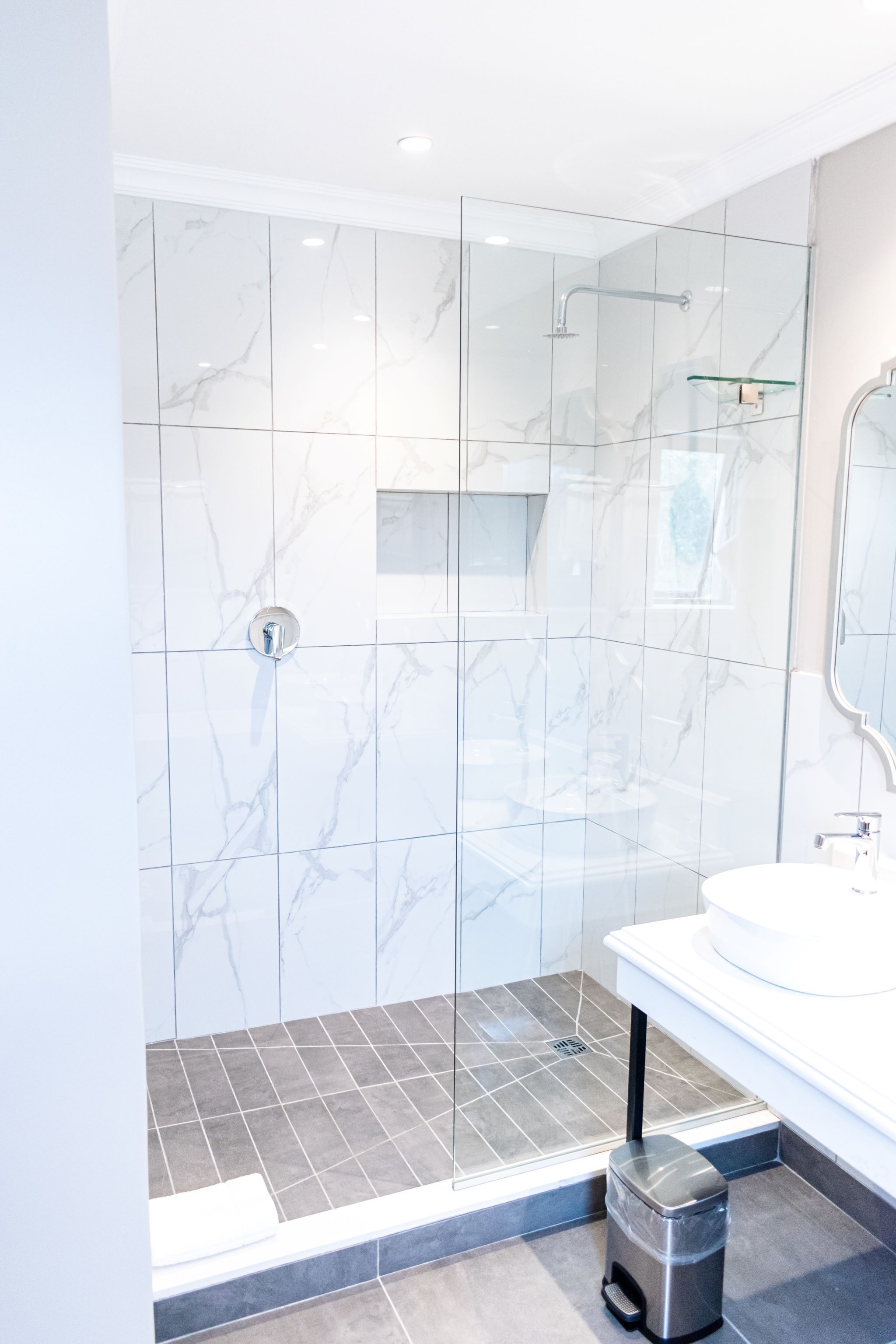 Un baño moderno con ducha de vidrio, lavabo blanco y un cubo de basura.