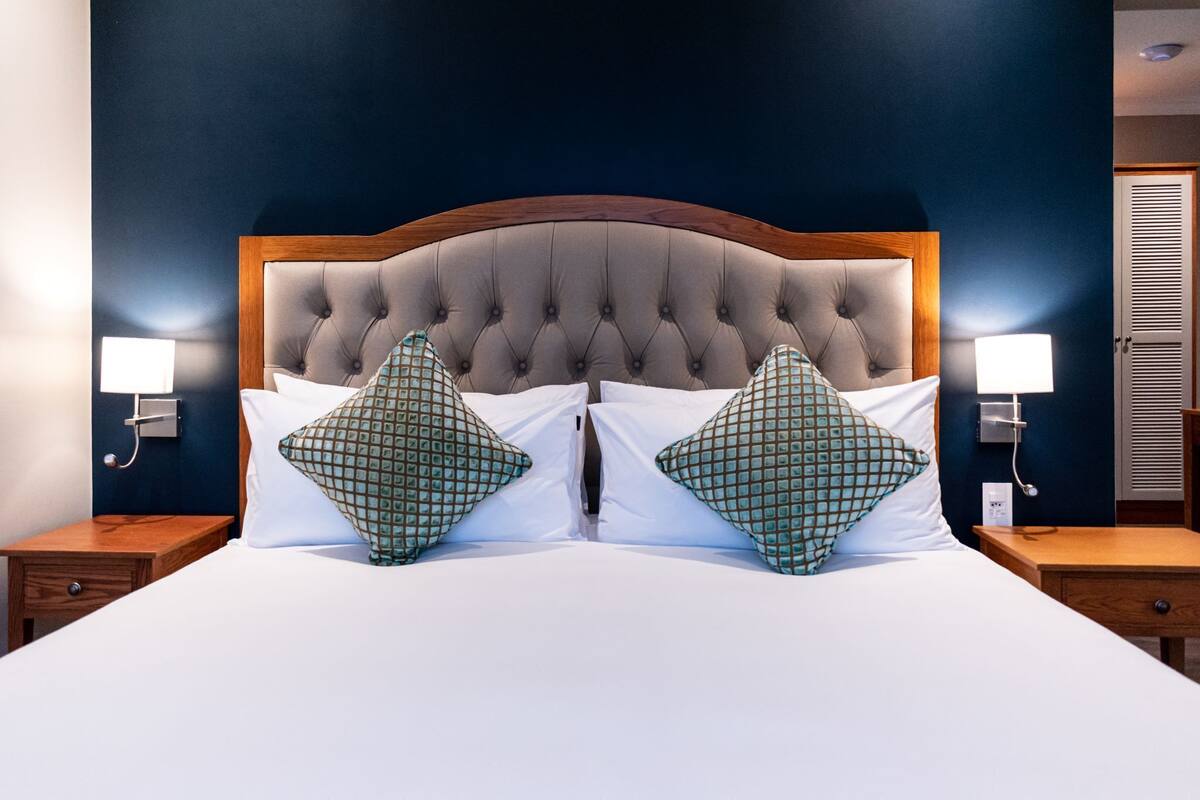A double bed with a tufted headboard, two bedside tables with lamps, and a dark blue wall.