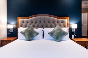 A double bed with a tufted headboard, two bedside tables with lamps, and a dark blue wall. - Premier Express Inn George (George)