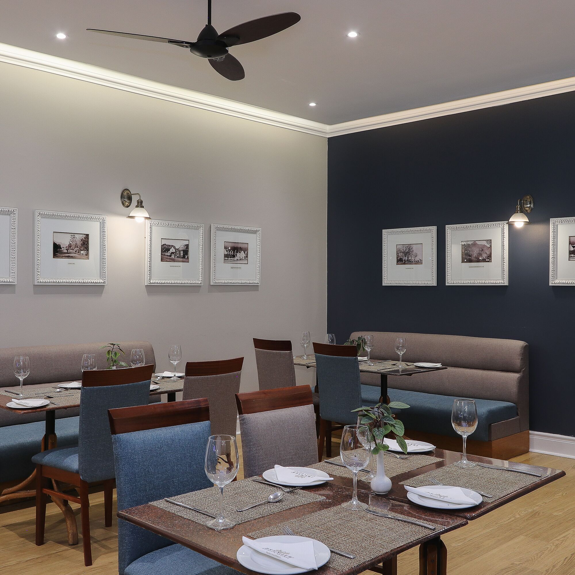 A dining area with tables set for two, chairs, and framed pictures on the wall.