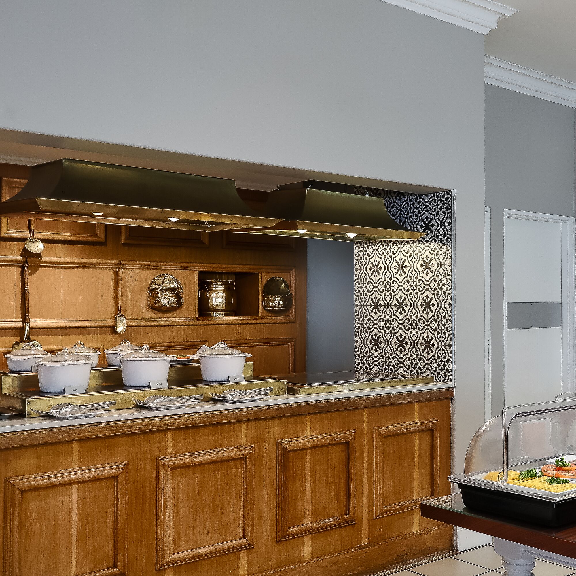 A kitchen with wooden cabinets, a stainless steel range hood, and a buffet counter with food items.
