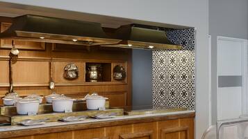 A kitchen with wooden cabinets, a stainless steel range hood, and a buffet counter with food items.