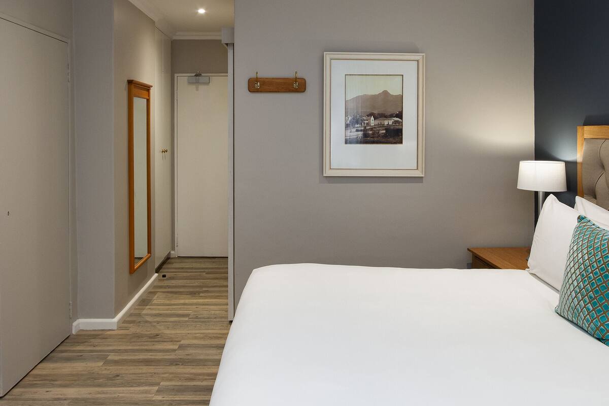 A hotel room with a bed, a nightstand, a lamp, a framed picture on the wall, and a wooden door.