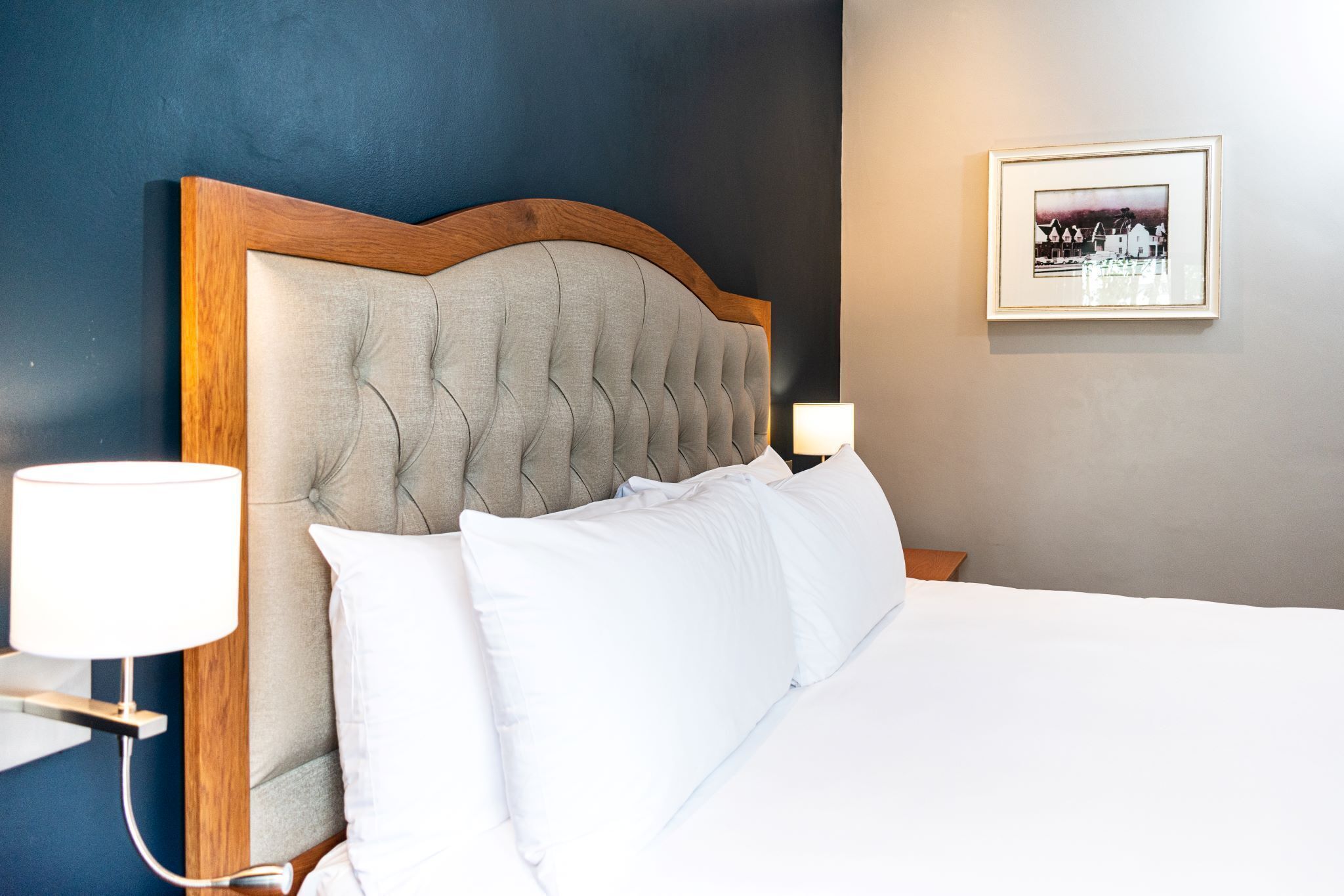 A neatly made bed with a wooden headboard, white bedding, and a bedside lamp.