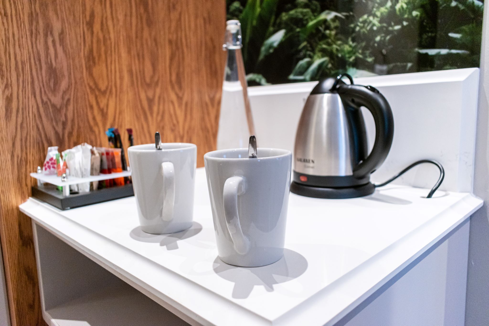 Two white mugs on a white countertop with a kettle and a tray of items in the background.