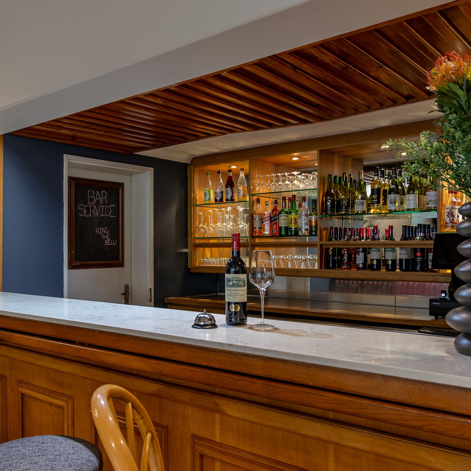 Una zona de bar con techo de madera, un menú en pizarra y una variedad de botellas y vasos en estantes.