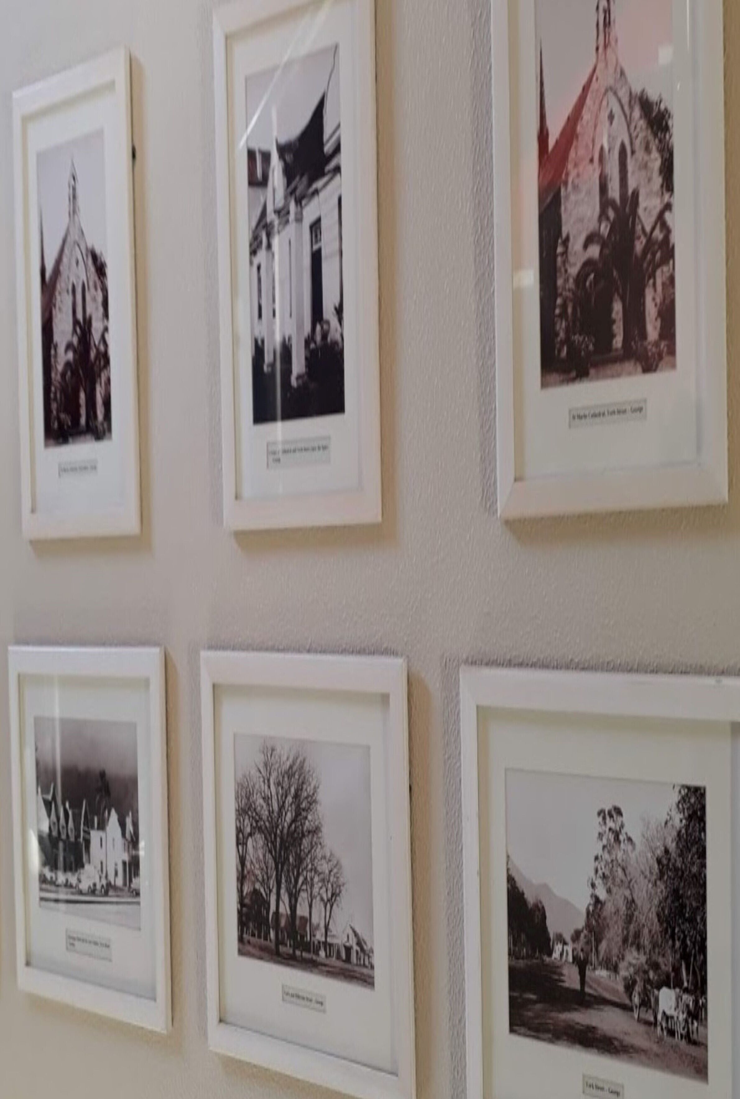 Een muur met zes ingelijste zwart-witfoto's van gebouwen en landschappen.