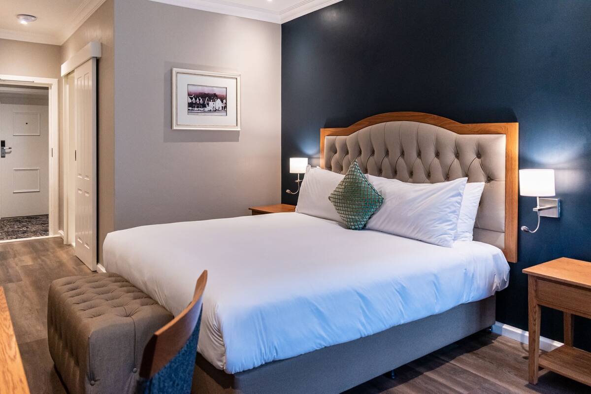 A neatly made bed with a tufted headboard, a bedside table with a lamp, and a framed picture on the wall.