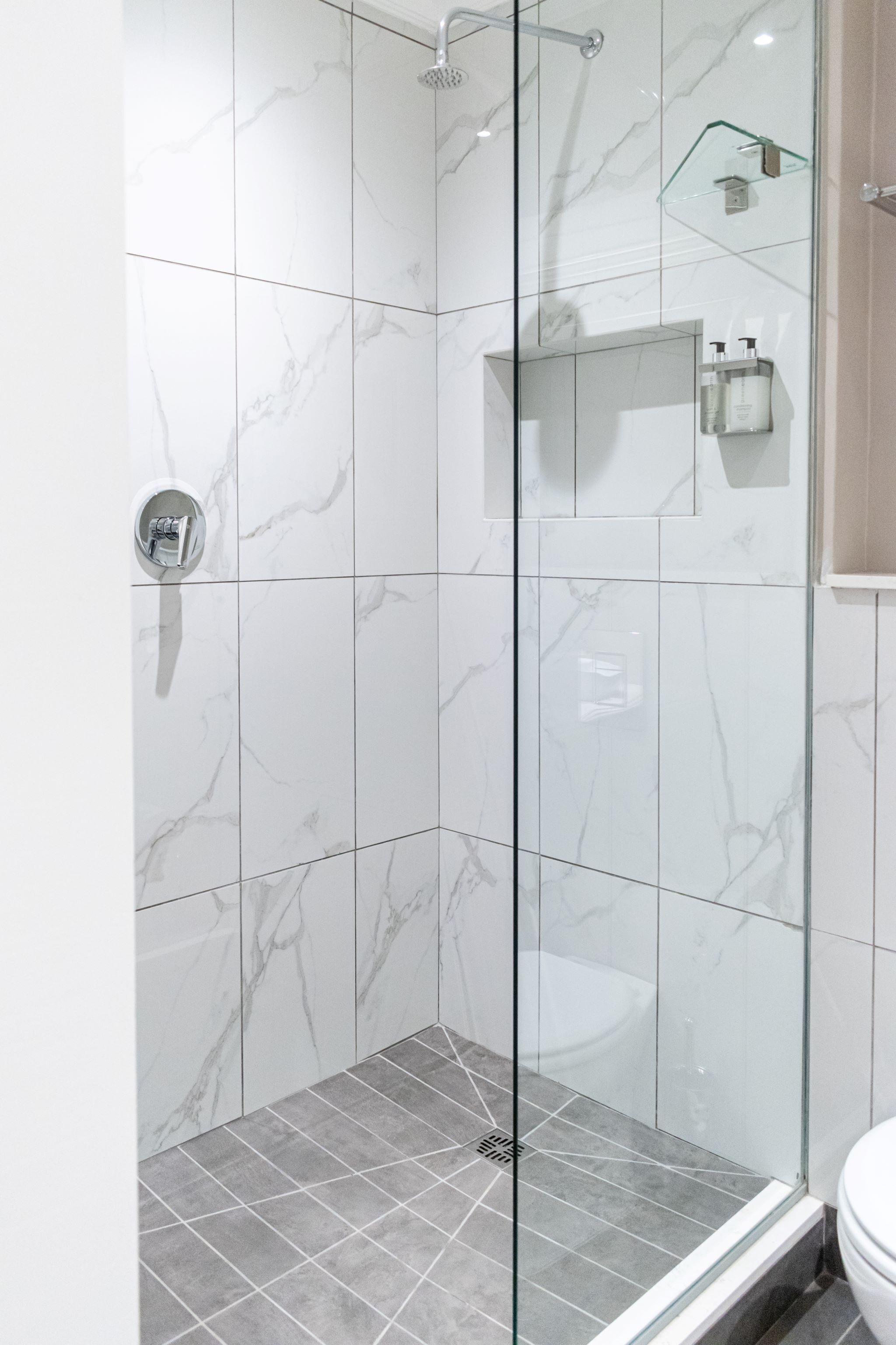 A modern bathroom with marble tiles, a glass shower enclosure, and a toilet.