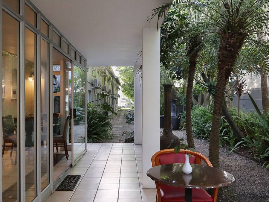 An outdoor patio area with a tiled floor, a glass door entrance, a small round table with a white vase, and red chairs.