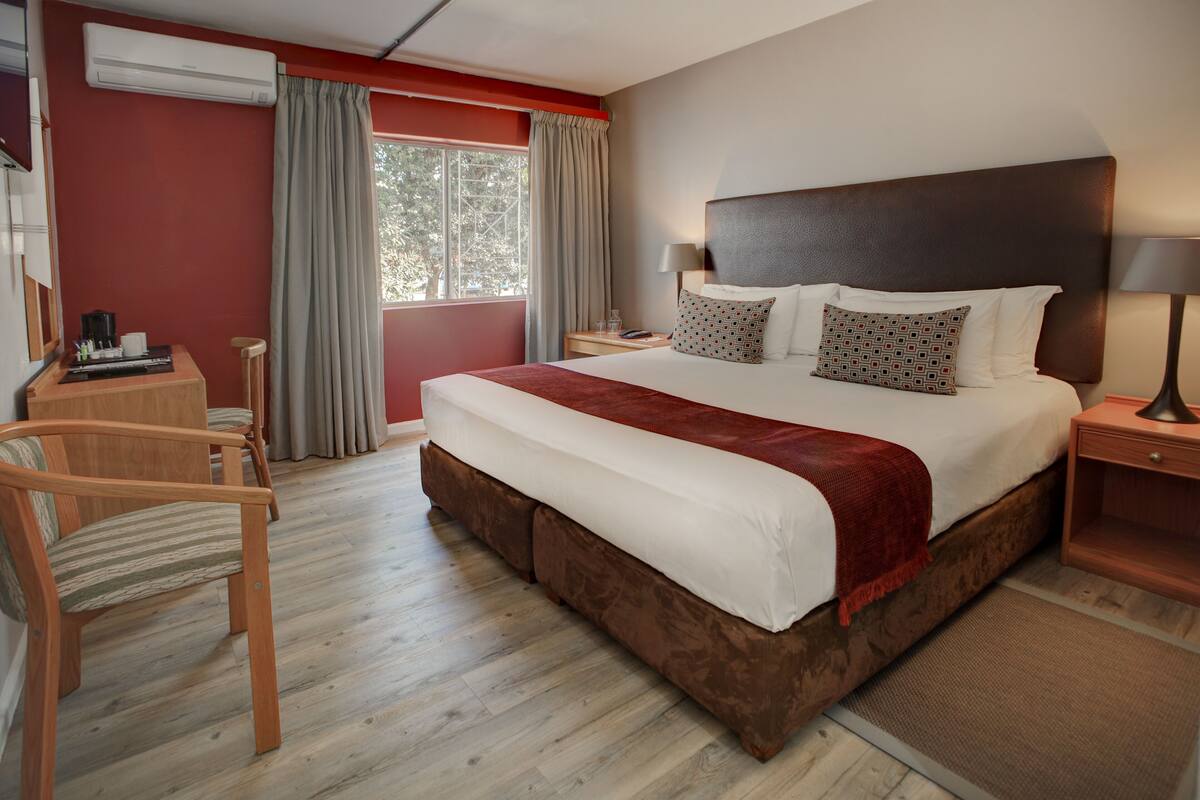 A hotel room with a large bed, a desk, a chair, and a window with curtains.