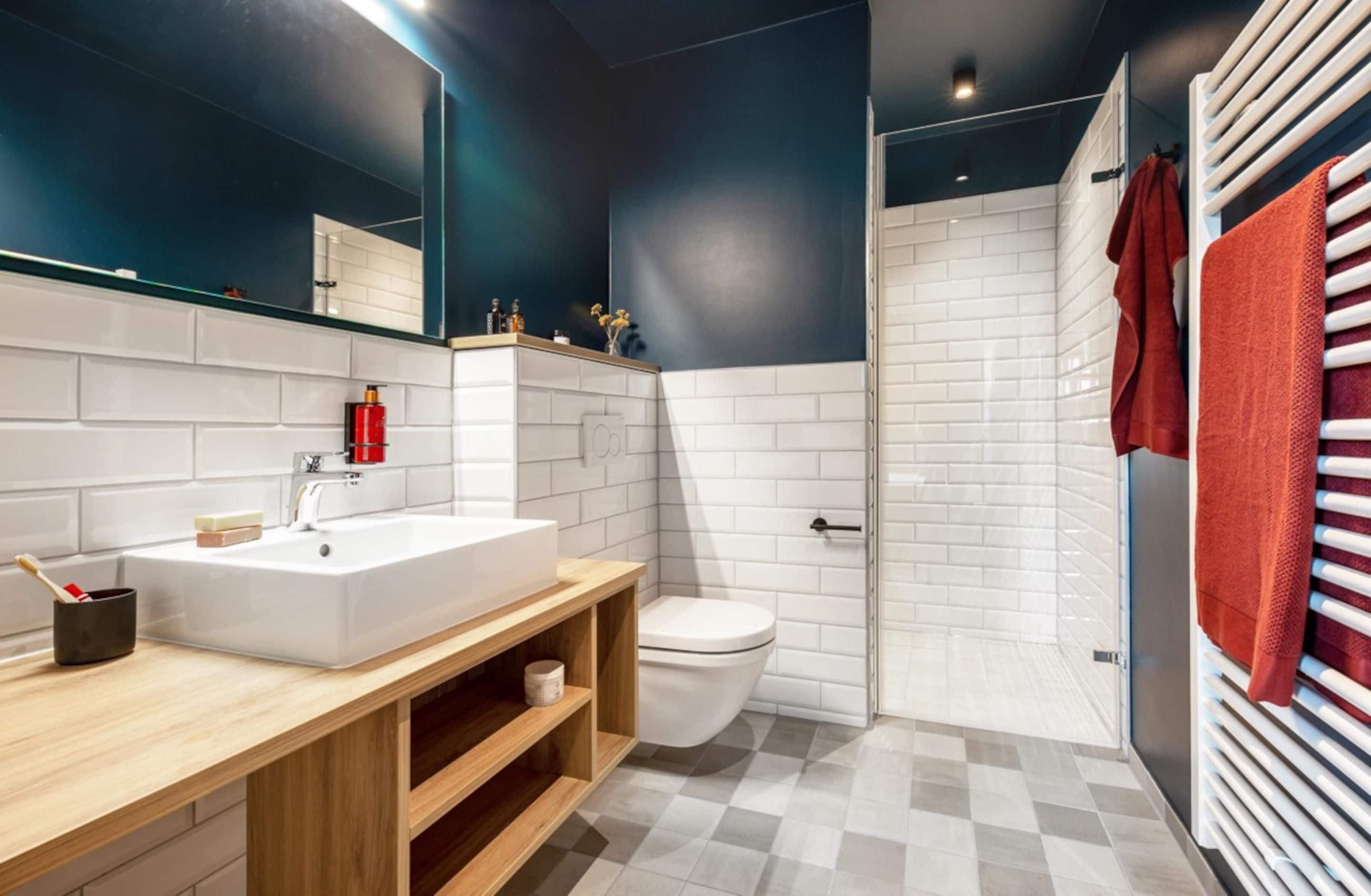 A modern bathroom with a white sink, wooden vanity, a toilet, and a shower area.