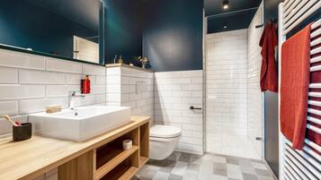 Un baño moderno con lavamanos blanco, tocador de madera, inodoro y zona de ducha.