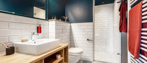A modern bathroom with a white sink, wooden vanity, a toilet, and a shower area.
