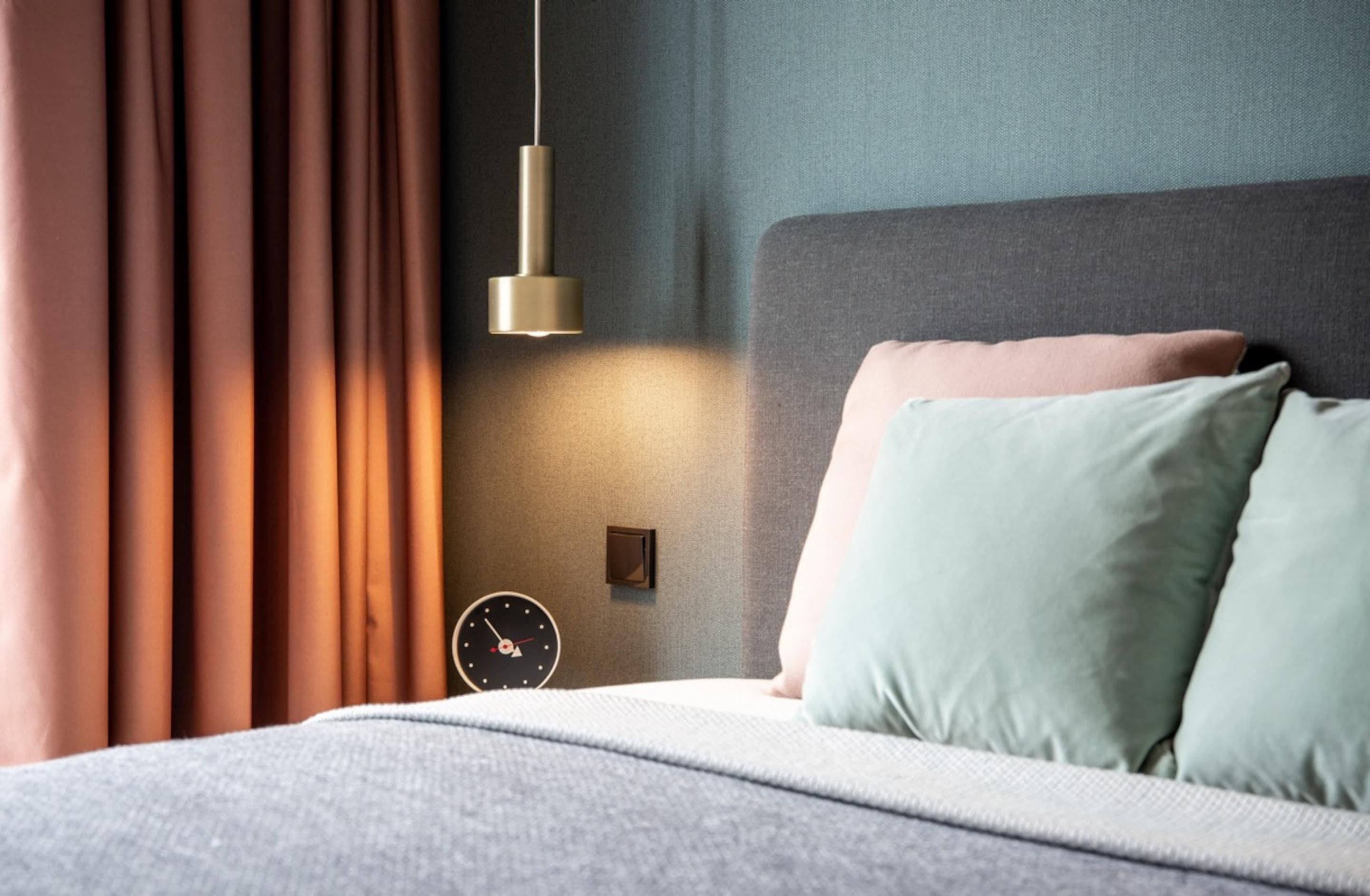 Cama bem arrumada com almofadas, um relógio na parede e um lustre em um quarto moderno.