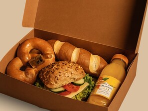 A box containing a pretzel, a loaf of bread, a sandwich, a bottle of mustard, and a bottle of salad dressing. - ipartment Braunschweig @HOME by Best Western (Braunschweig)
